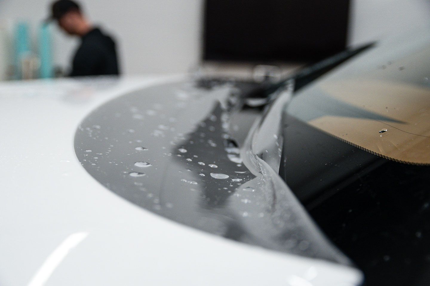 A person applying film to a car's windshield, likely for protection. Focus is on the film, with water droplets visible.