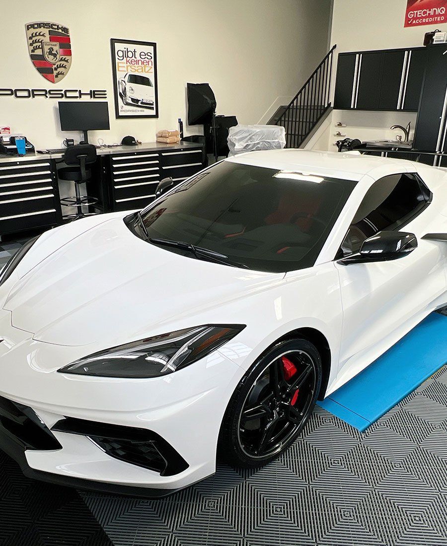 Red Ferrari sports car centered in a bright white garage with reflective flooring.