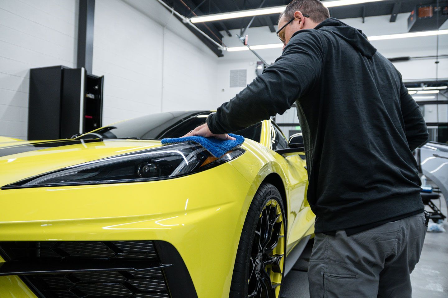 A man is cleaning a yellow sports car in a garage.