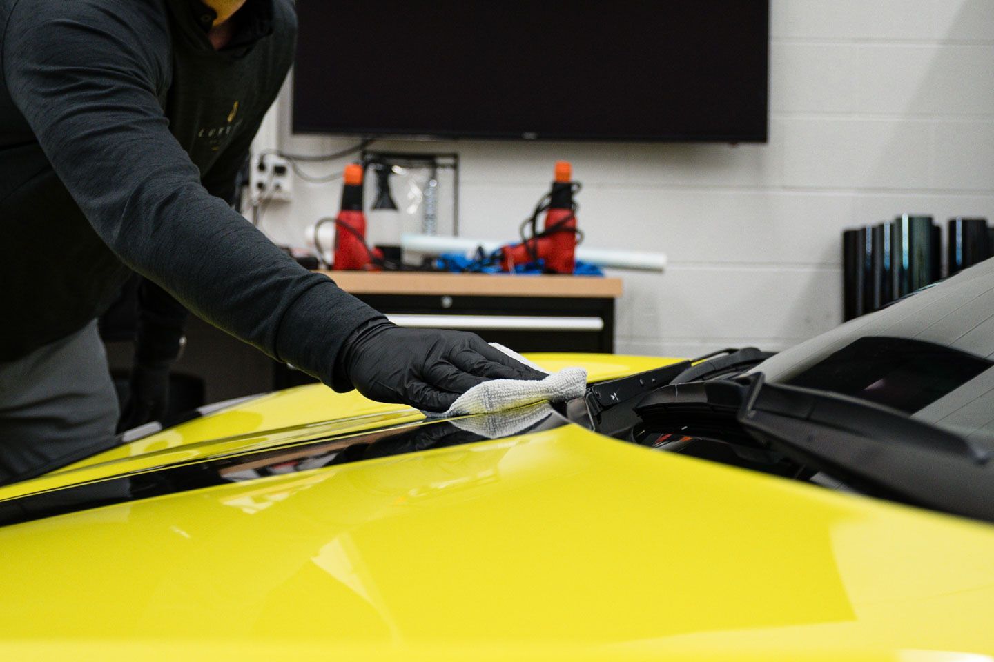 A man is cleaning the hood of a yellow car with a cloth.