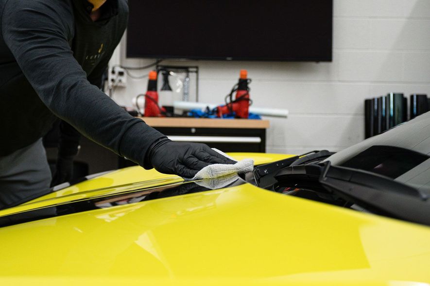 A man is cleaning the hood of a yellow car with a cloth.