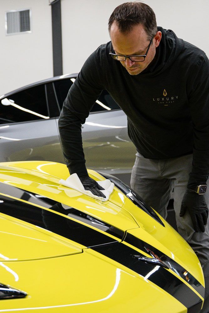 A man is cleaning the hood of a yellow sports car.