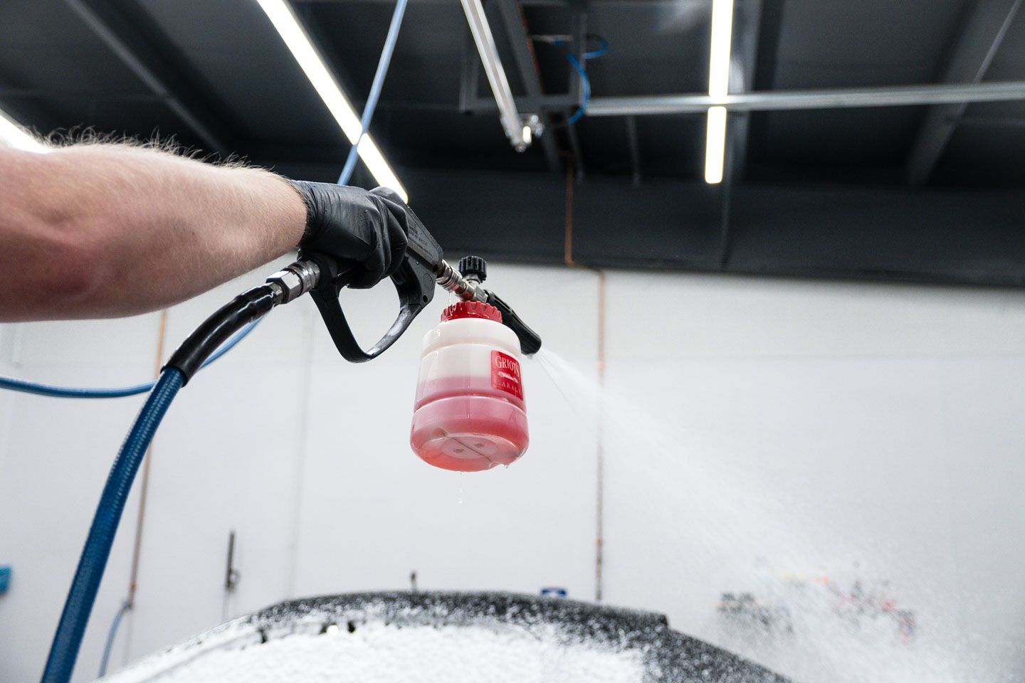 Person spraying red liquid from a foam cannon onto a car in a garage.