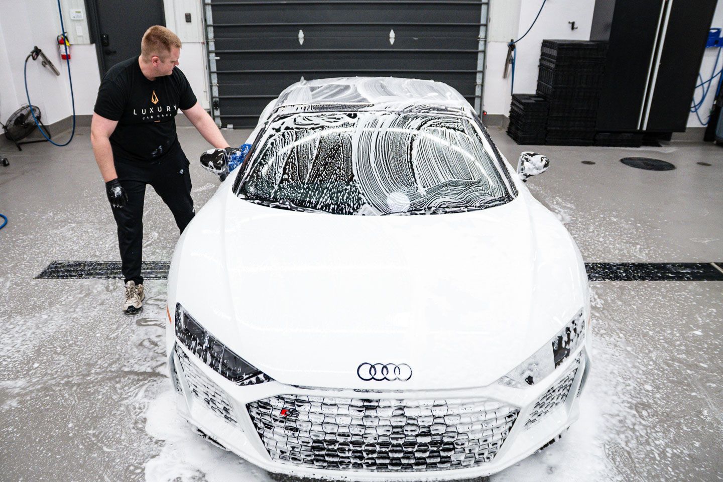 A man is washing a white audi r8 with foam.