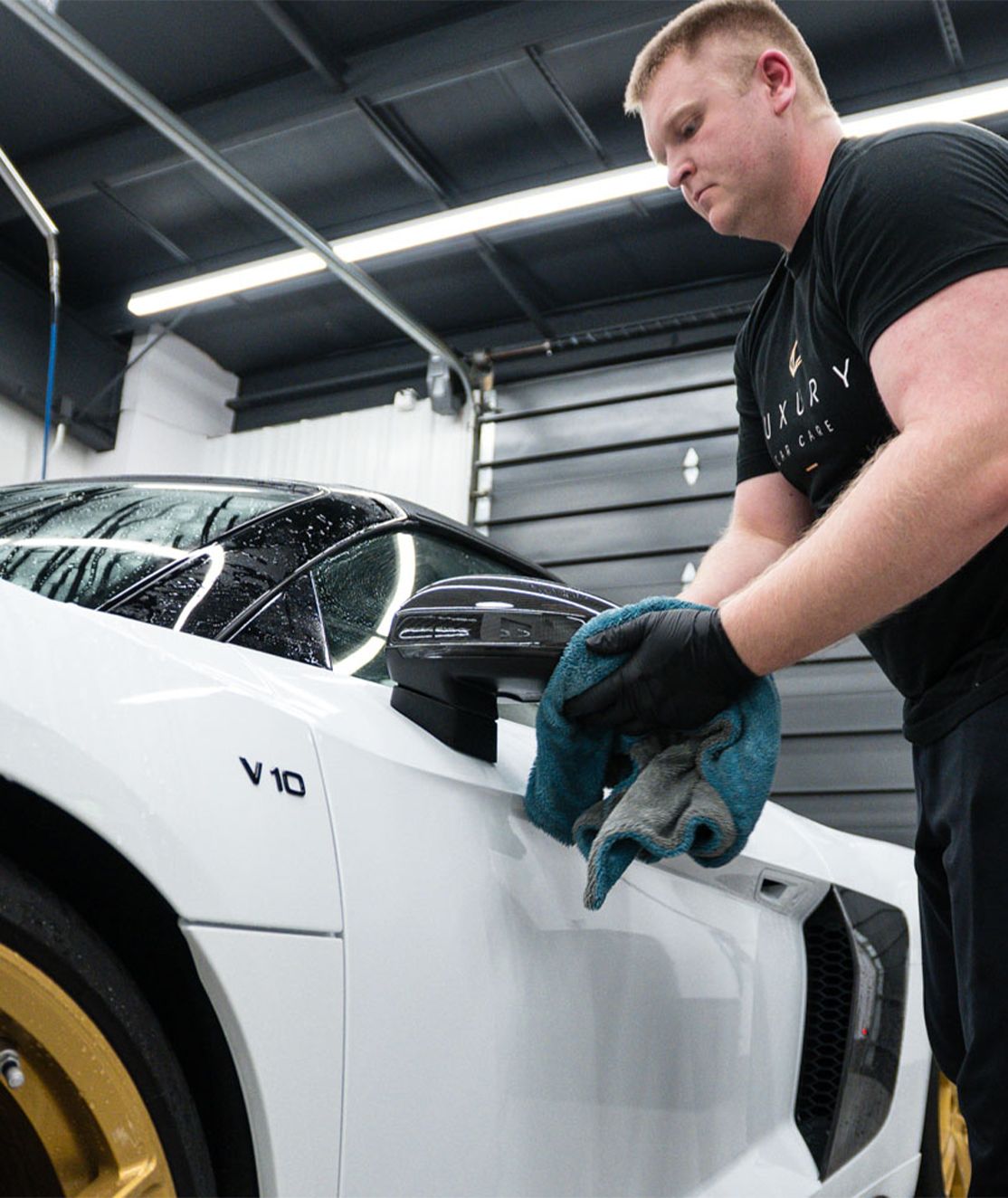 A man is cleaning a white sports car with a cloth.