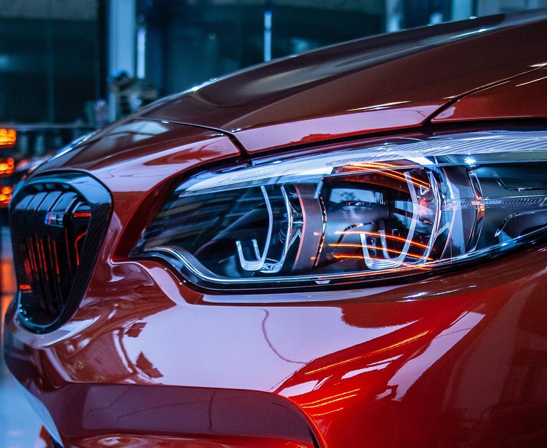 Close-up of a red sports car headlight and grill. The car is glossy and reflects lights.