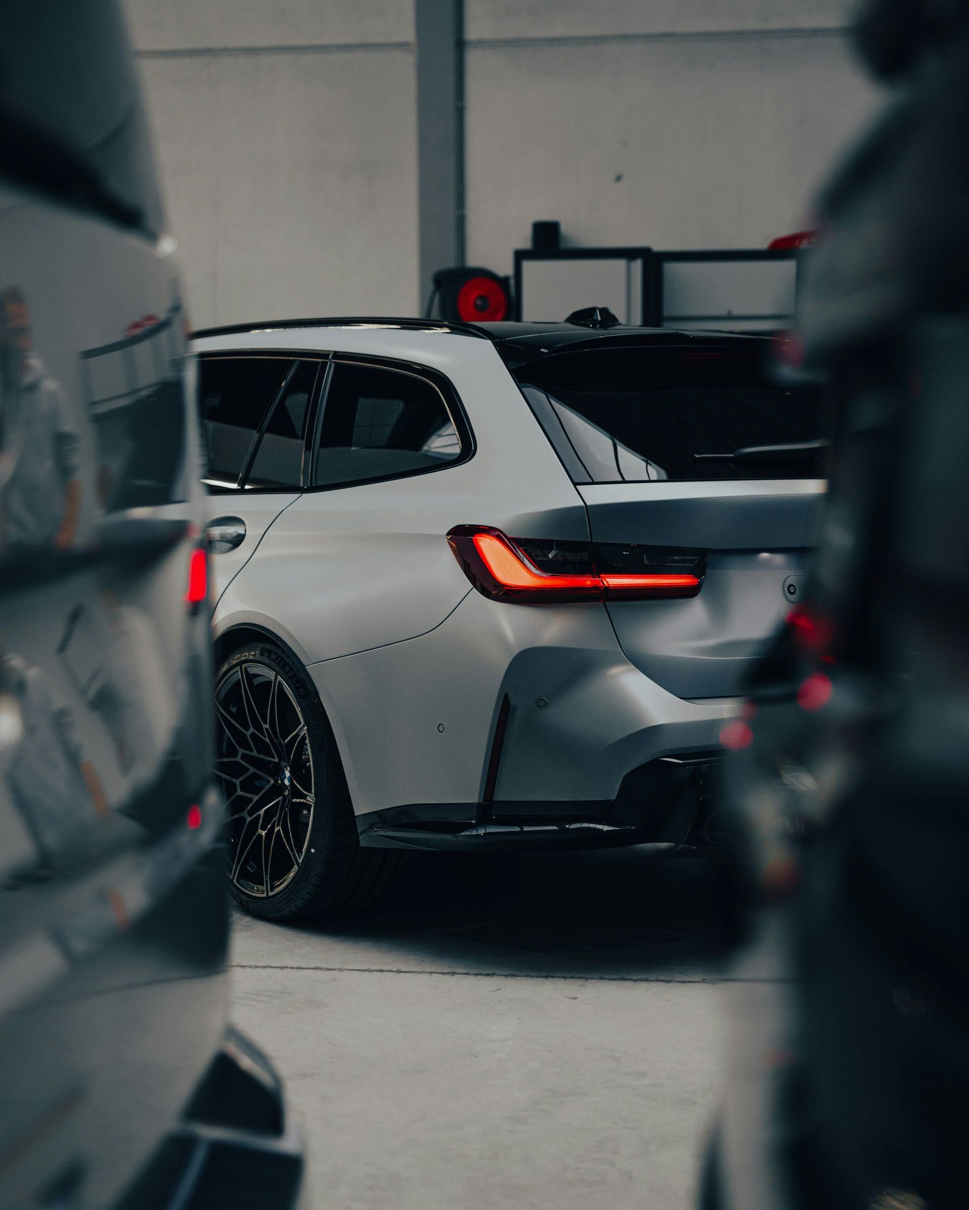 Gray BMW station wagon parked in a garage, viewed from the rear. Black wheels and red taillights are visible.