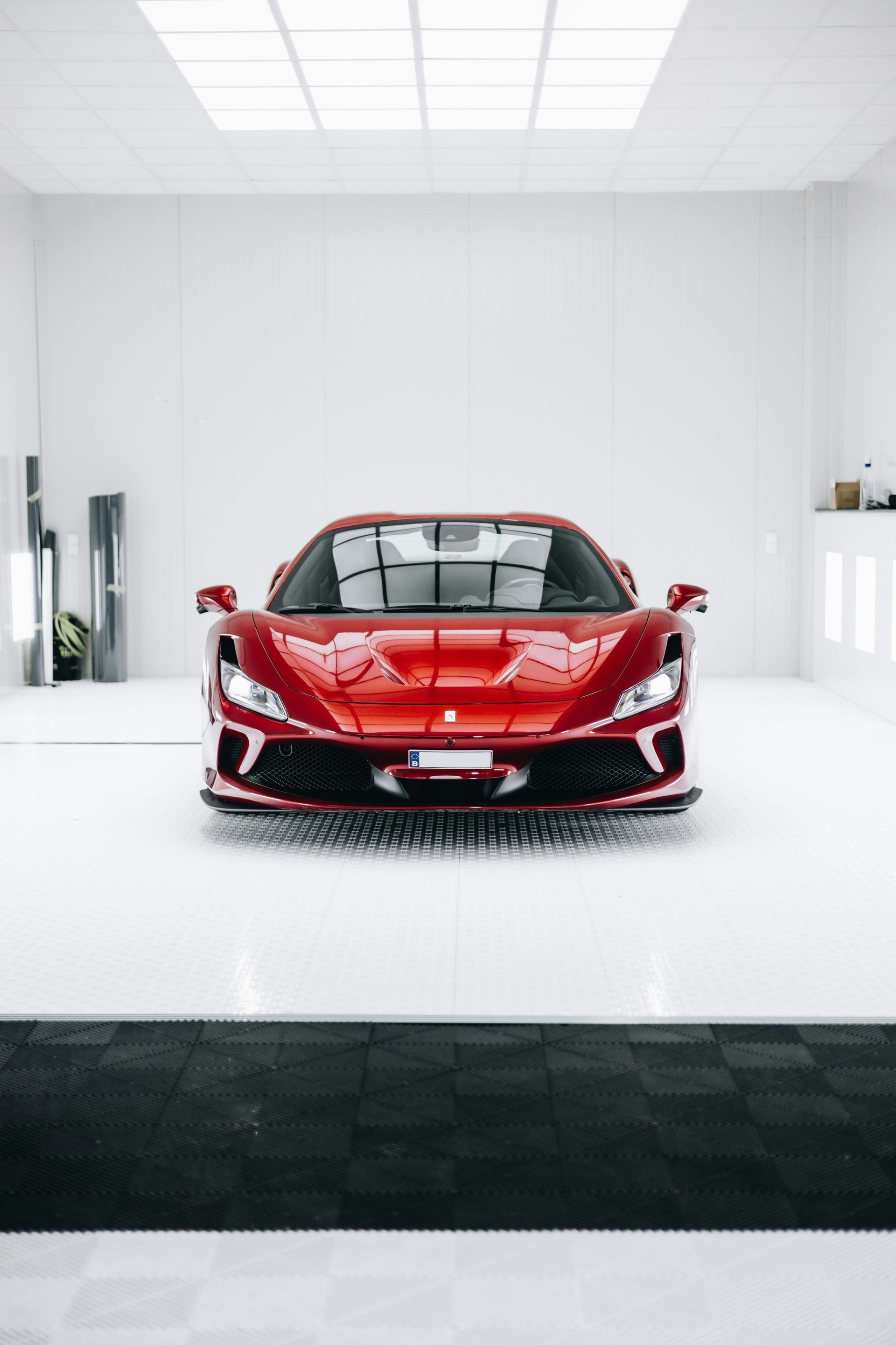 Red Ferrari sports car centered in a bright white garage with reflective flooring.