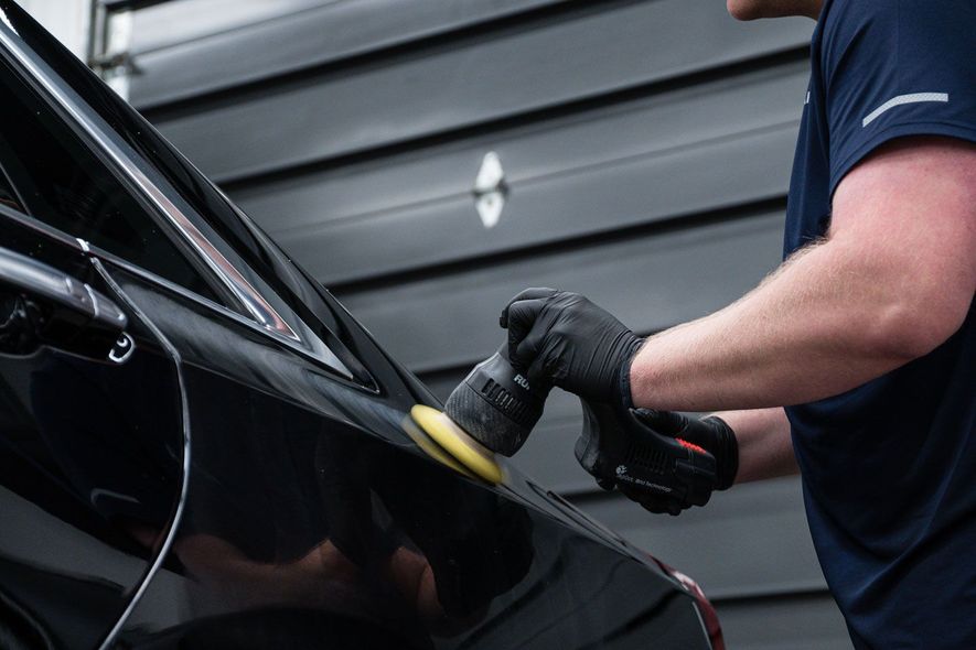 A man is polishing a black car with a polisher.