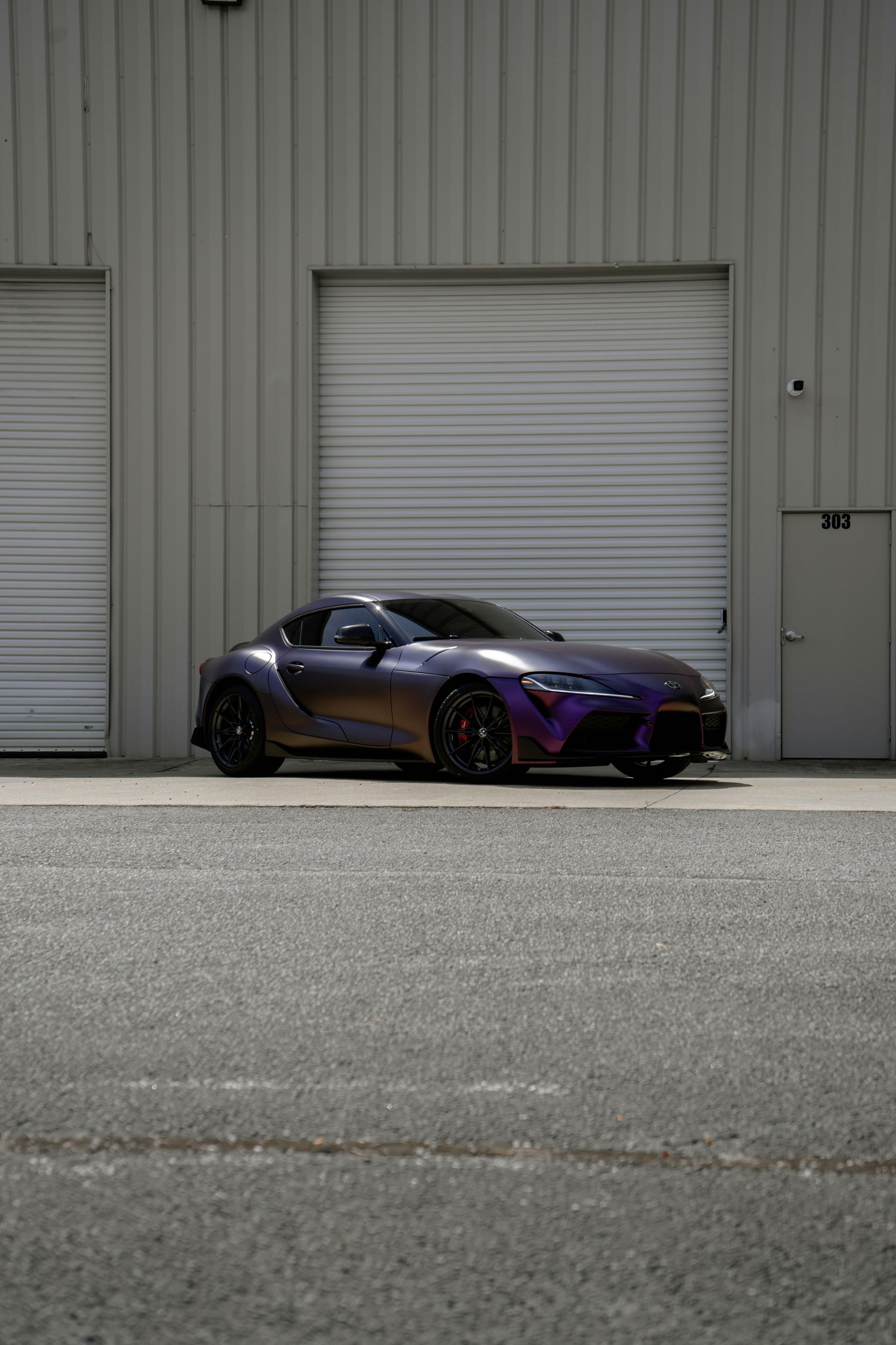 Purple and black sports car parked in front of a gray warehouse with closed garage doors.