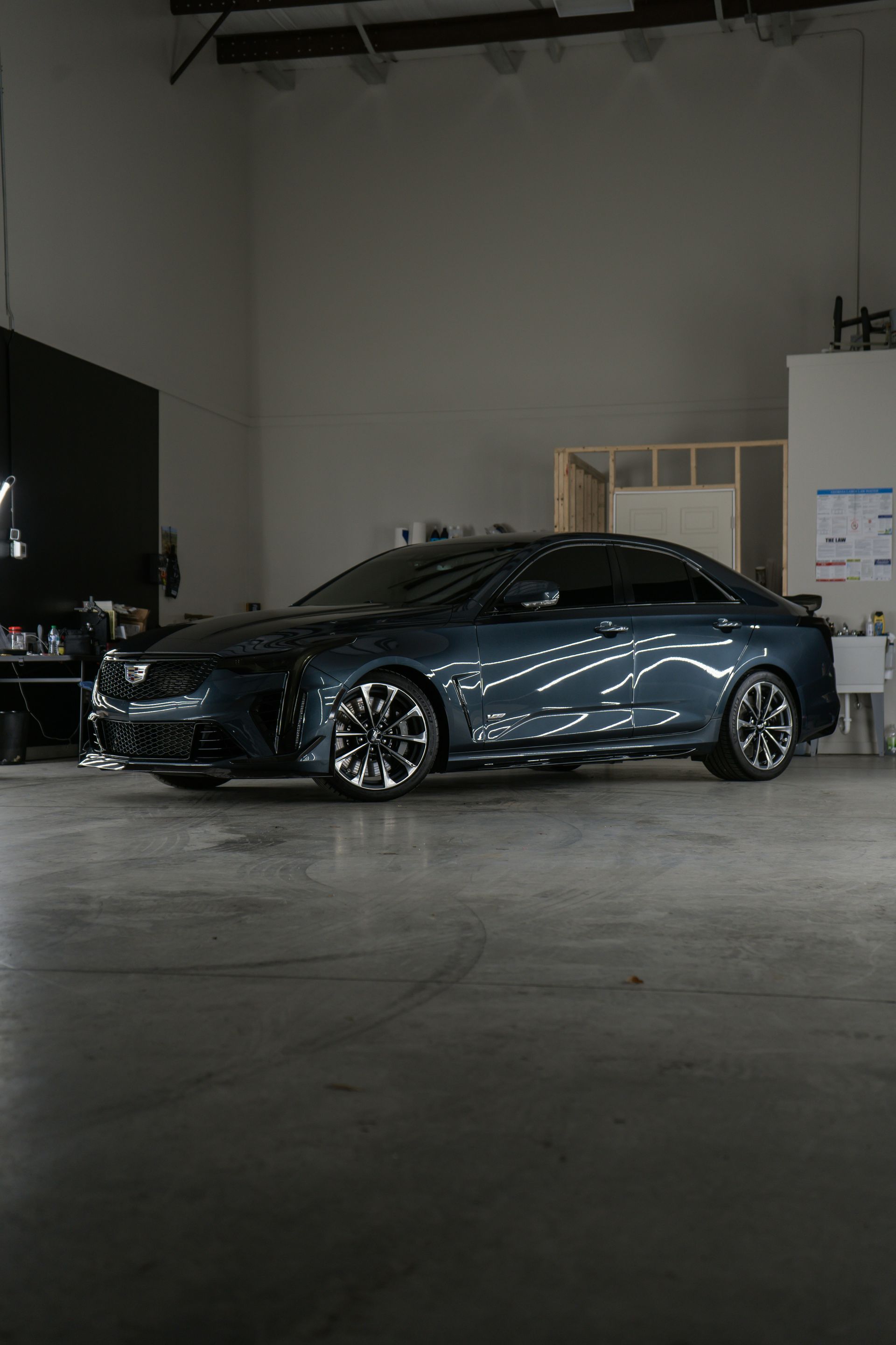 Dark blue Cadillac sedan in a studio setting, shiny wheels, parked near a structure.