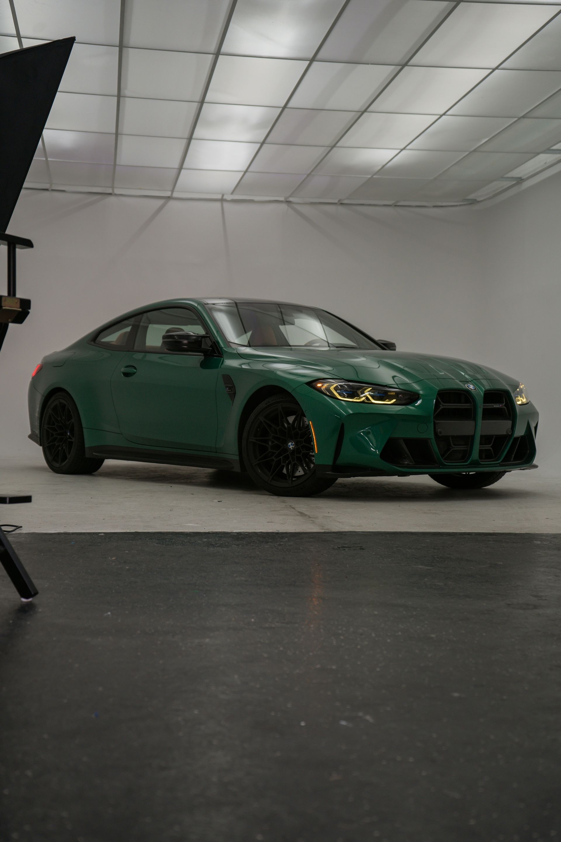 Green BMW M4 coupe parked in a white studio. Black wheels, sleek design.