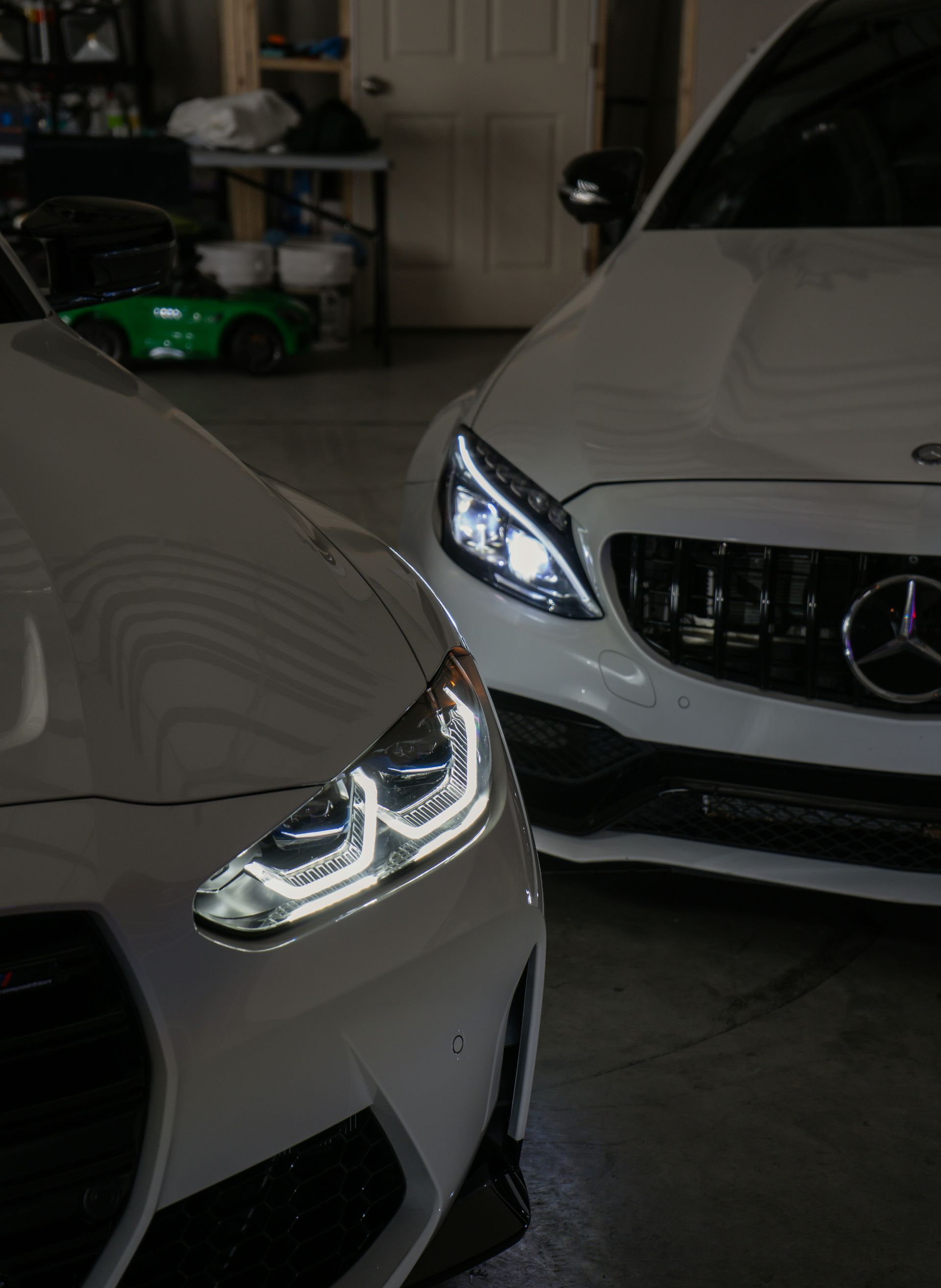 Two white cars, a DS 3 Crossback and a Mercedes-Benz C-Class, parked in a garage. Their headlights are illuminated.