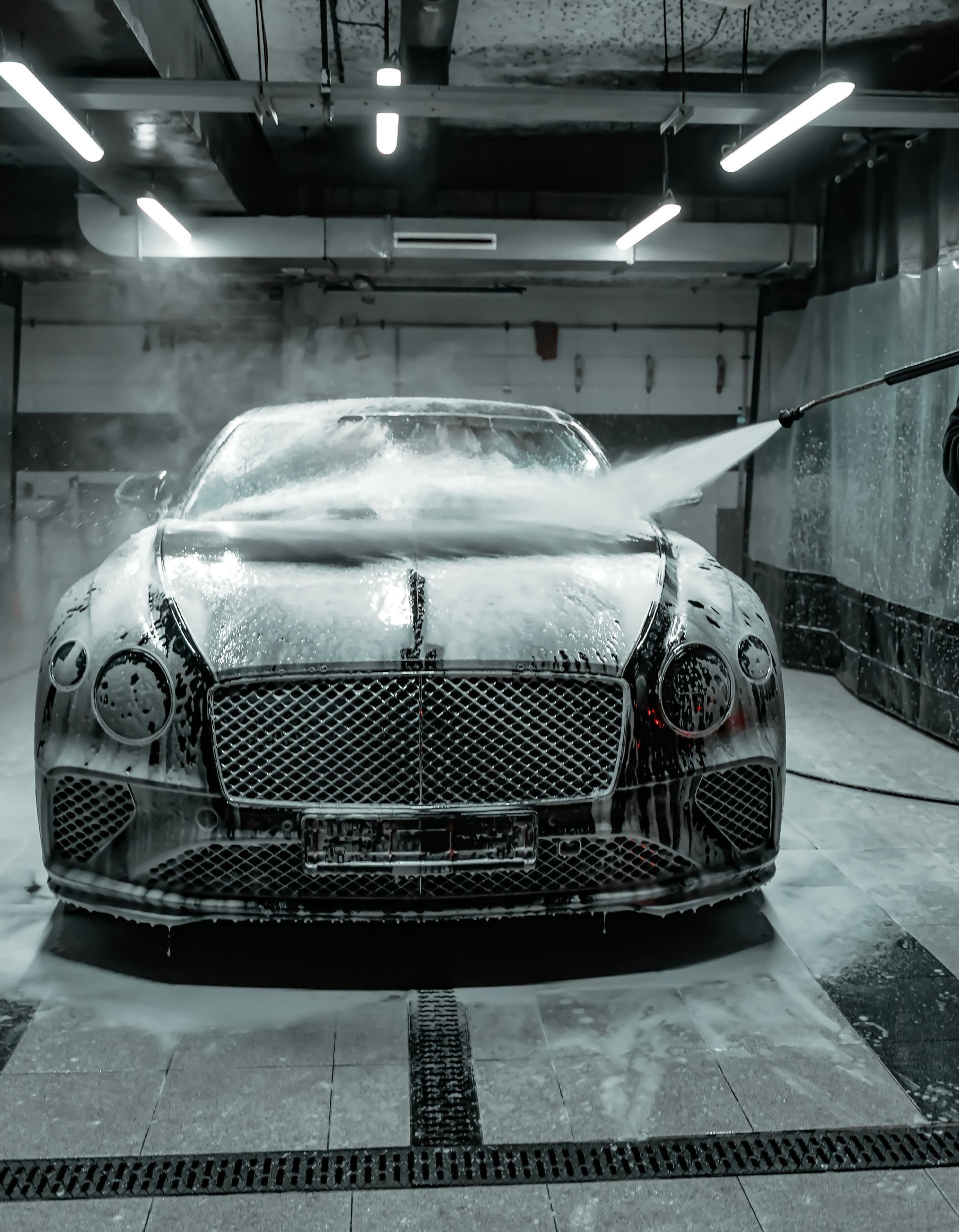 Bentley being washed with soapy water at a car wash, spray covers front of the car.