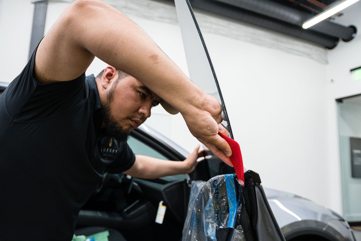 A man is wrapping a car window with a red tape.