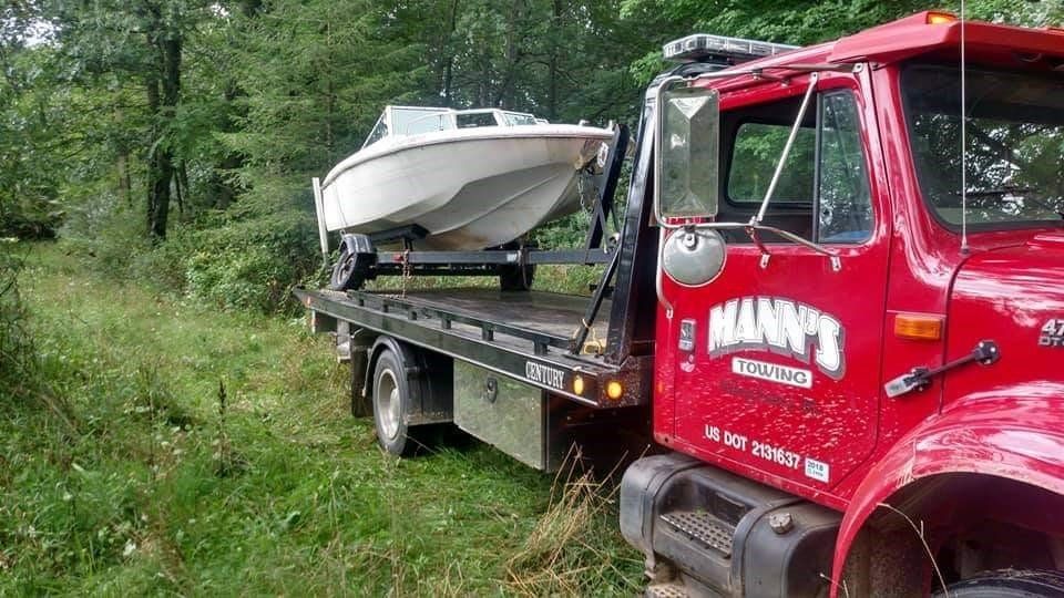 a red tow truck is carrying a boat on the back of it .