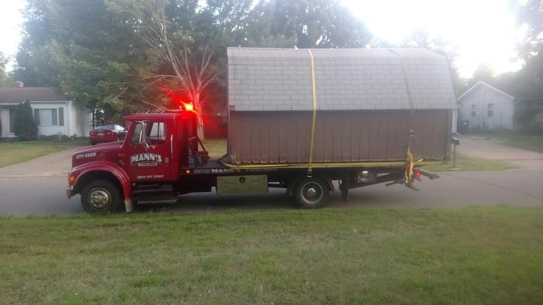 a red tow truck is carrying a shed on the back of it .