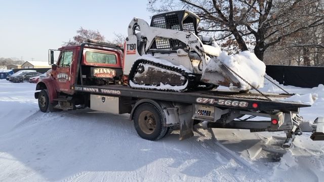 a tow truck is carrying a bulldozer in the snow .
