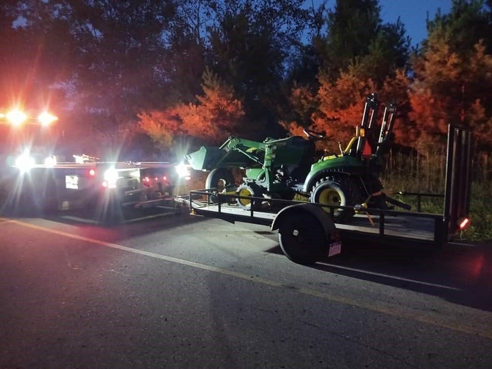 a green tractor is on a trailer on the side of the road at night .