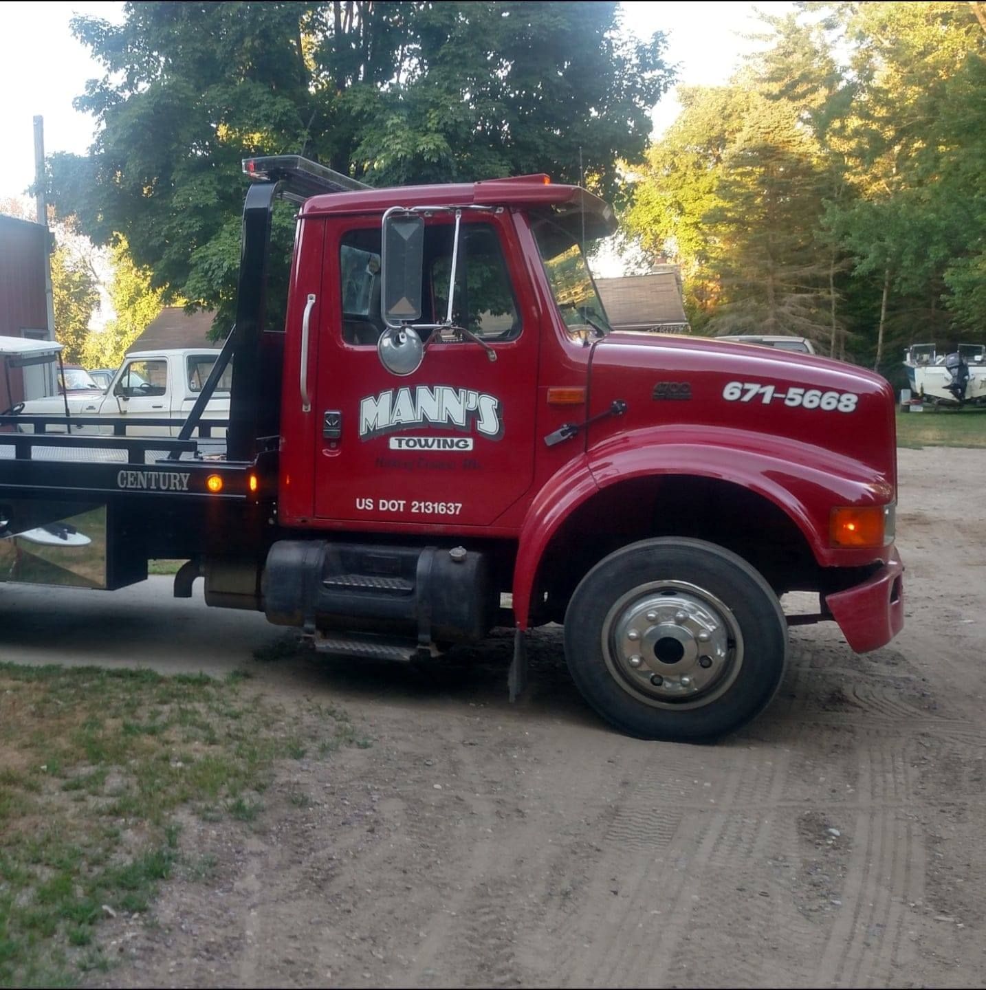 a red mann 's tow truck is parked in the dirt