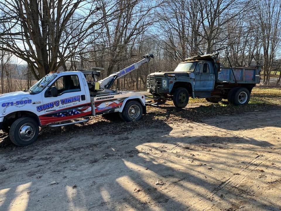 a tow truck is towing a dump truck on a dirt road .