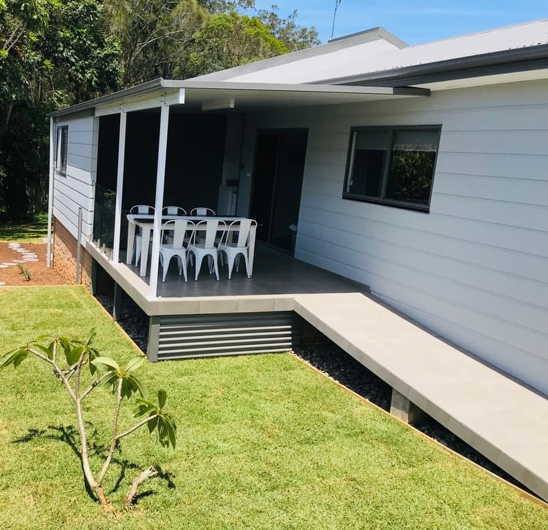 Exterior view of a white building with a covered porch and a concrete ramp for accessibility.