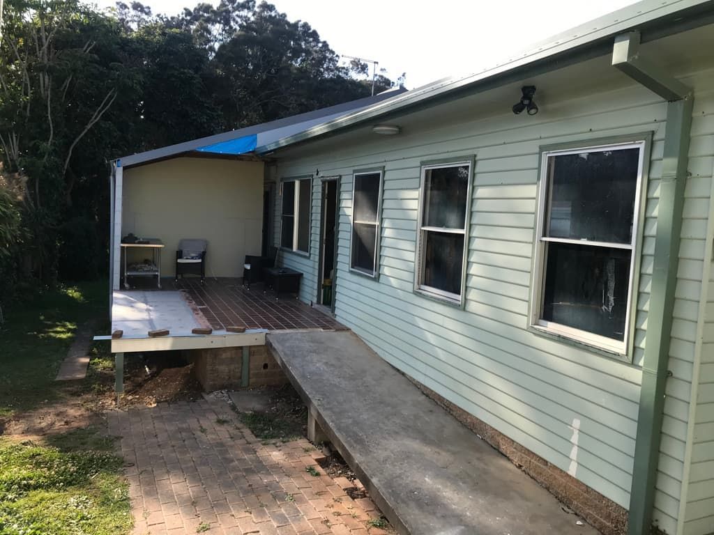 Side view of a light green house with a wooden deck and a concrete ramp for accessibility.