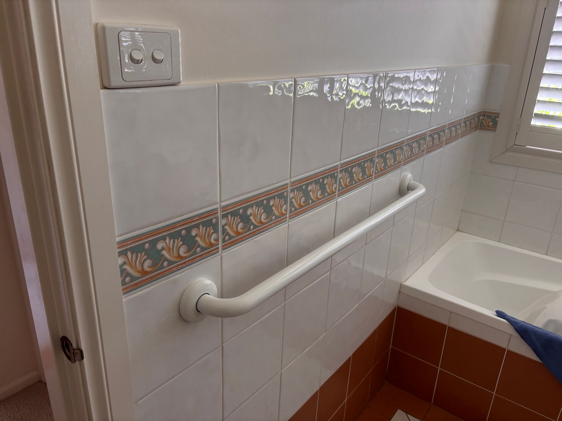 A white bathroom grab bar installed horizontally on a tiled wall next to a bathtub.