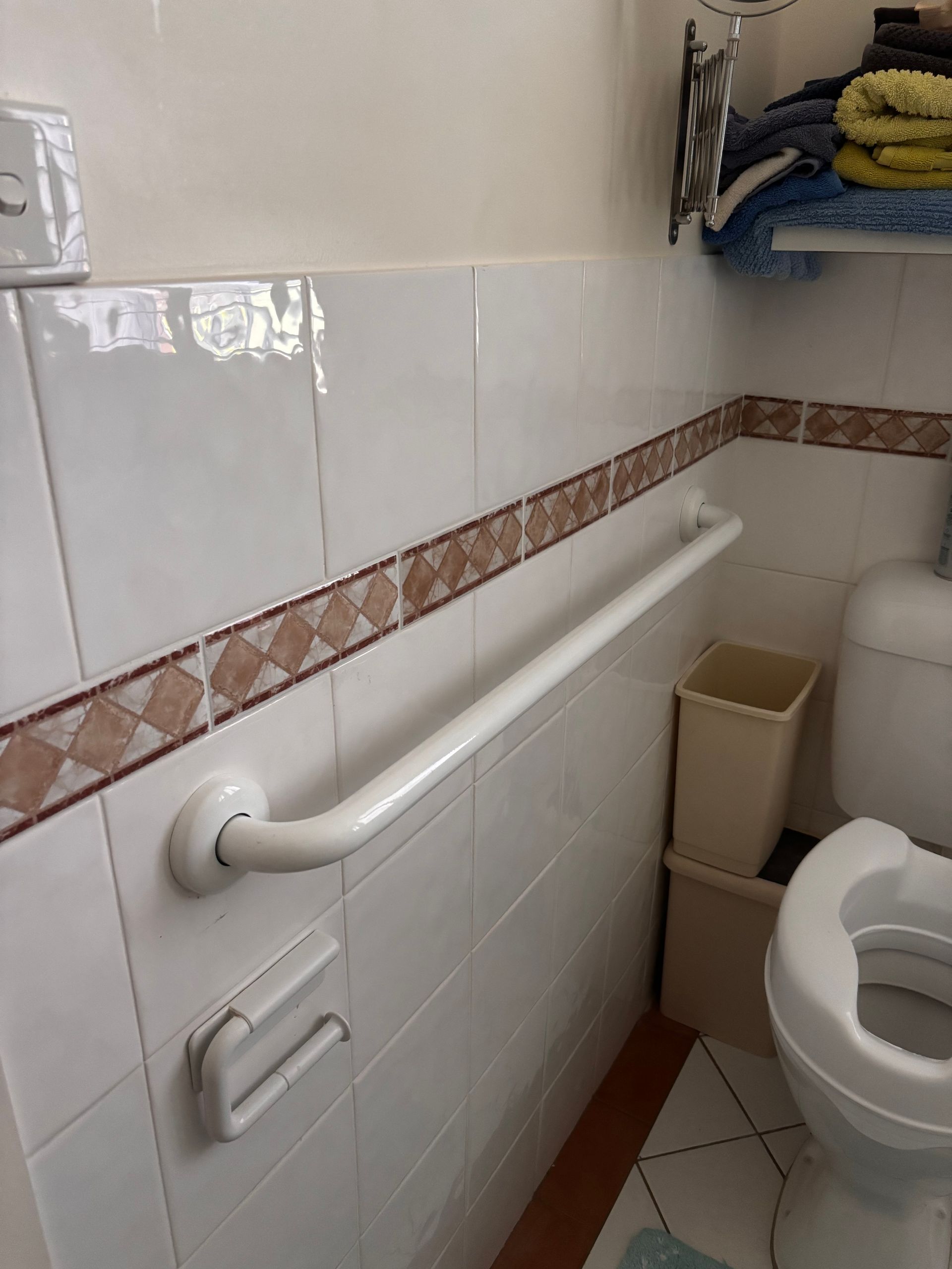 White safety grab bar mounted horizontally on a tiled bathroom wall next to a white toilet.