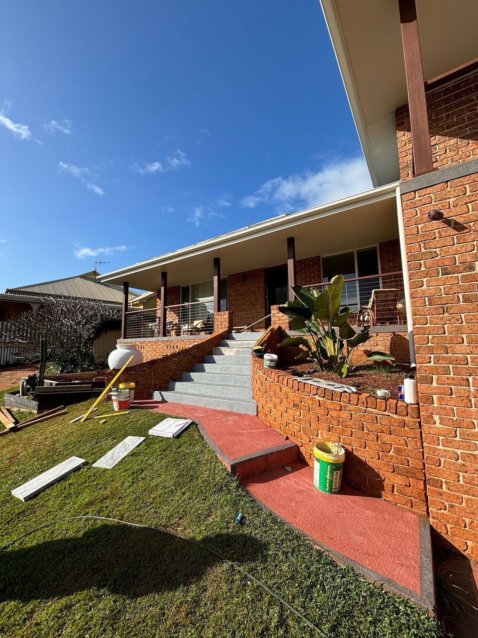A red brick house with a front porch, stairs, and a red pathway leading to the entrance under a clear blue sky.