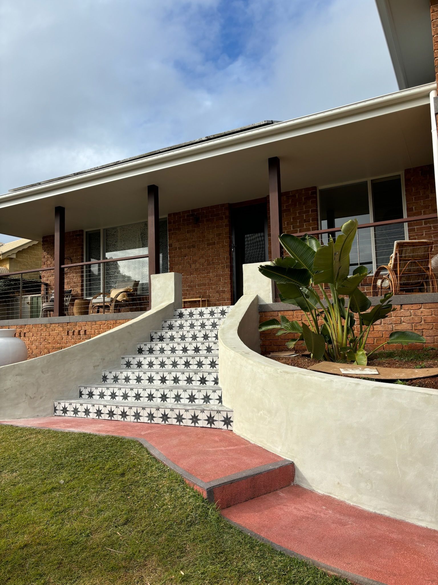 Stairs with decorative black and white patterned tiles lead up to a brick house porch with a curved stucco retaining wall.