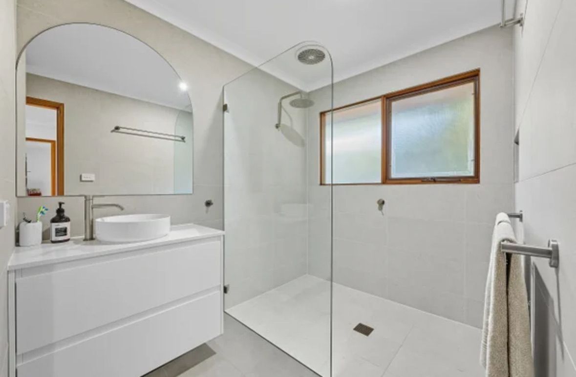 Modern White Bathroom With a Glass Shower, Vanity, and Arched Mirror — Edmonds Bathroom Renovations & Tiling In Wauchope, NSW
