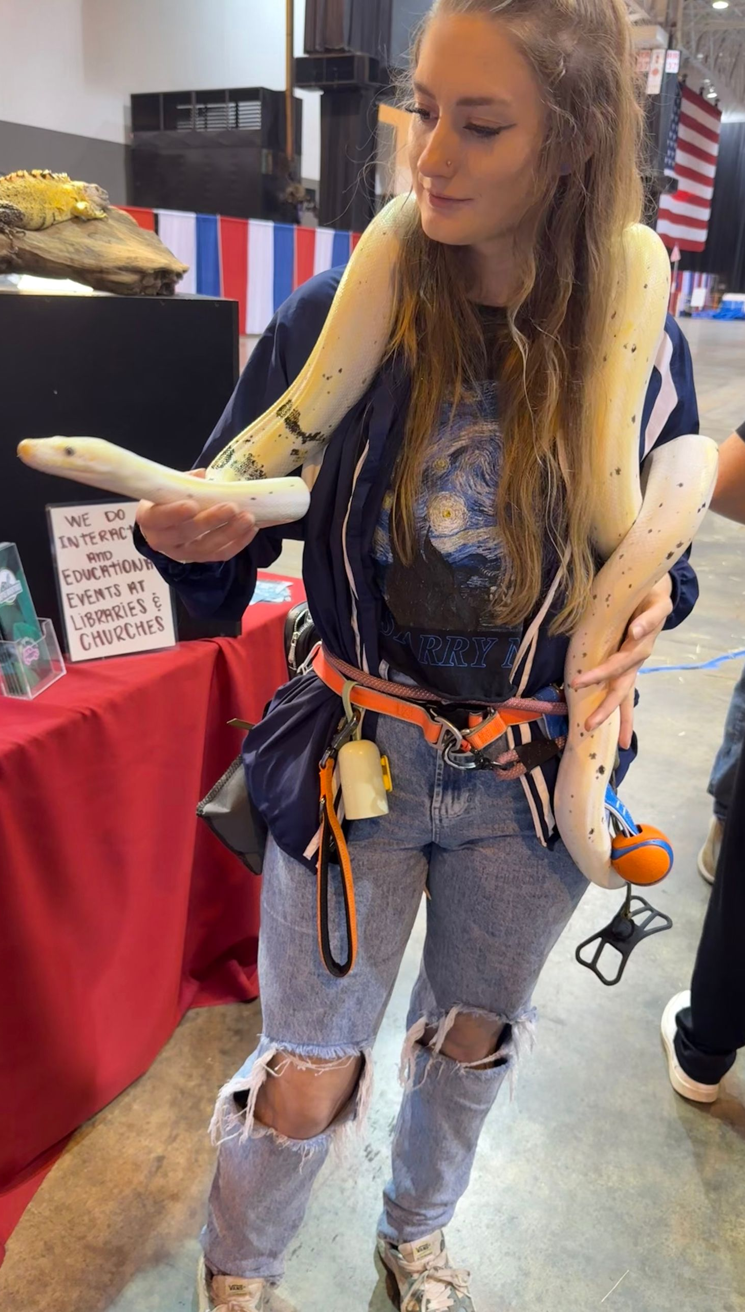 Lex with a white- yellow snake draped around her neck at a booth, wearing jeans and a jacket.