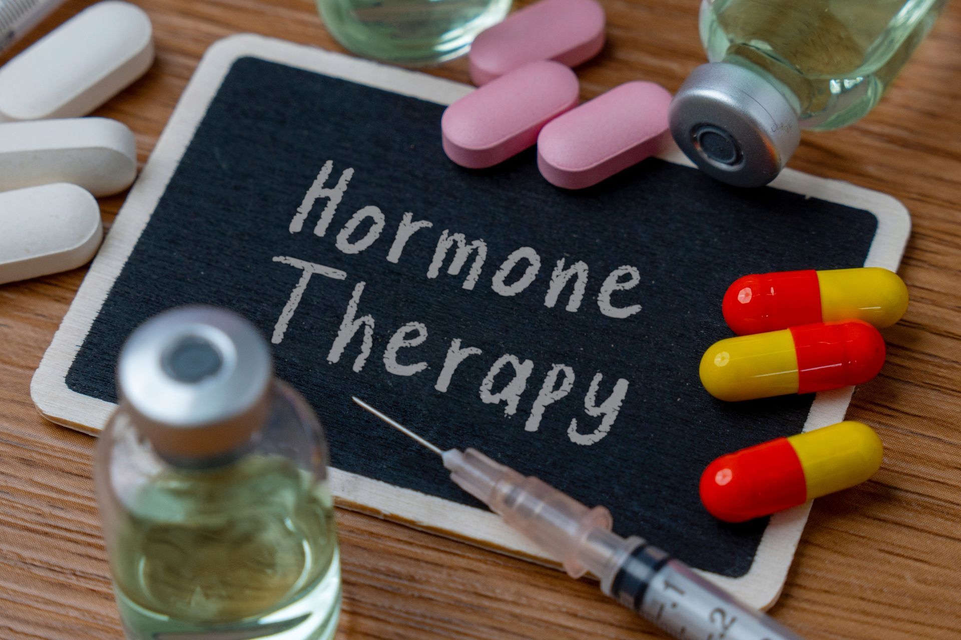 Small chalkboard with the words “Hormone Therapy,” with pills, capsules, vials, & a syringe. Small chalkboard with the words “Hormone Therapy,” with pills, capsules, vials, & a syringe.