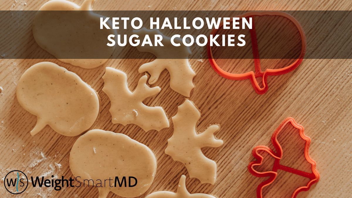 Keto Halloween sugar cookies, cut in pumpkin and bat shapes, on a wooden surface, with orange cookie cutters.