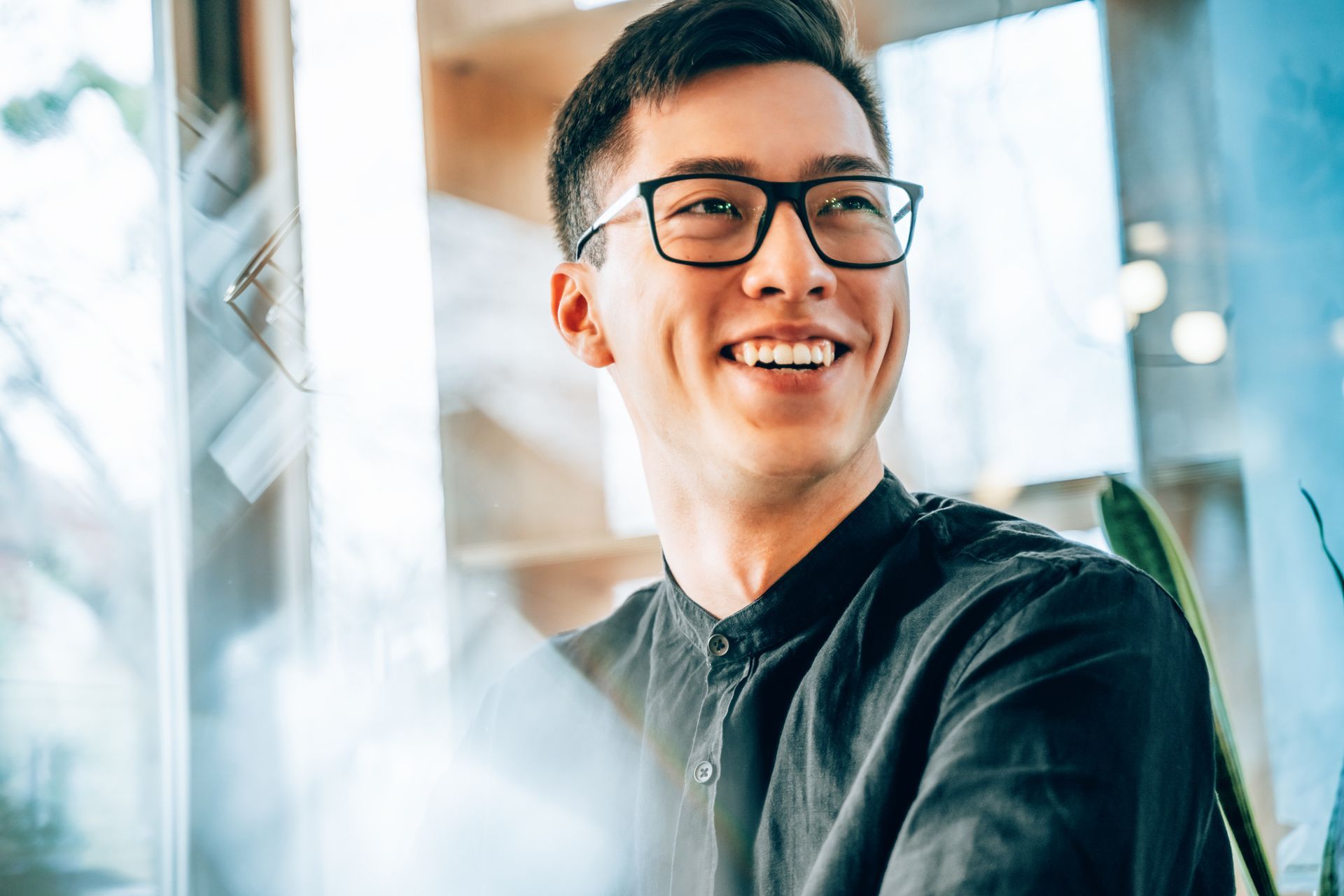 Smiling Asian man with glasses, wearing a black shirt, indoors.