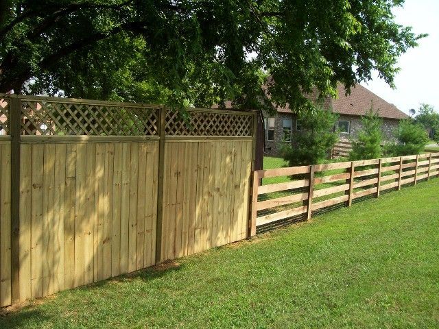 A solid privacy fence with a decorative lattice top next to a split-rail wooden fence in a grassy yard.