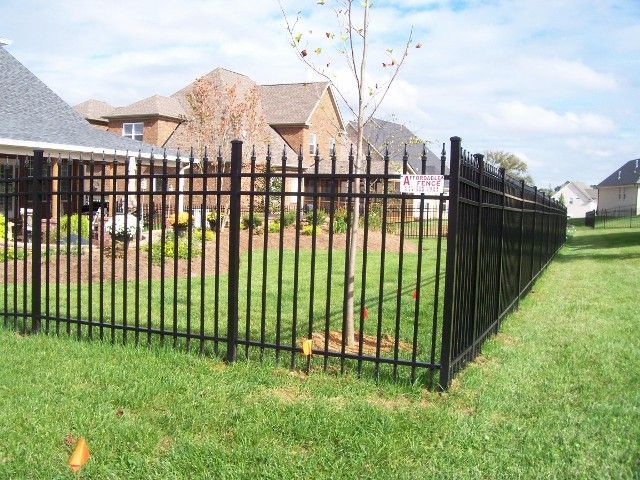 Black metal ornamental fence enclosing a grassy residential backyard with houses in the background.