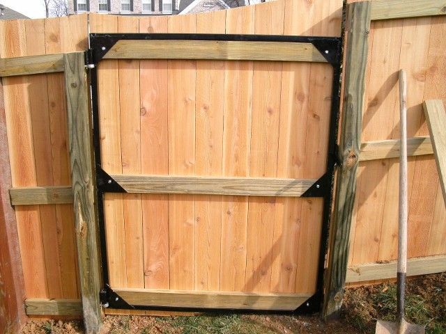 A wooden fence gate with a black metal frame support system attached to upright wooden posts.