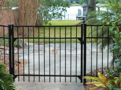 A wooden post-and-rail fence runs along a sloping grassy lawn in front of a brick and white house.