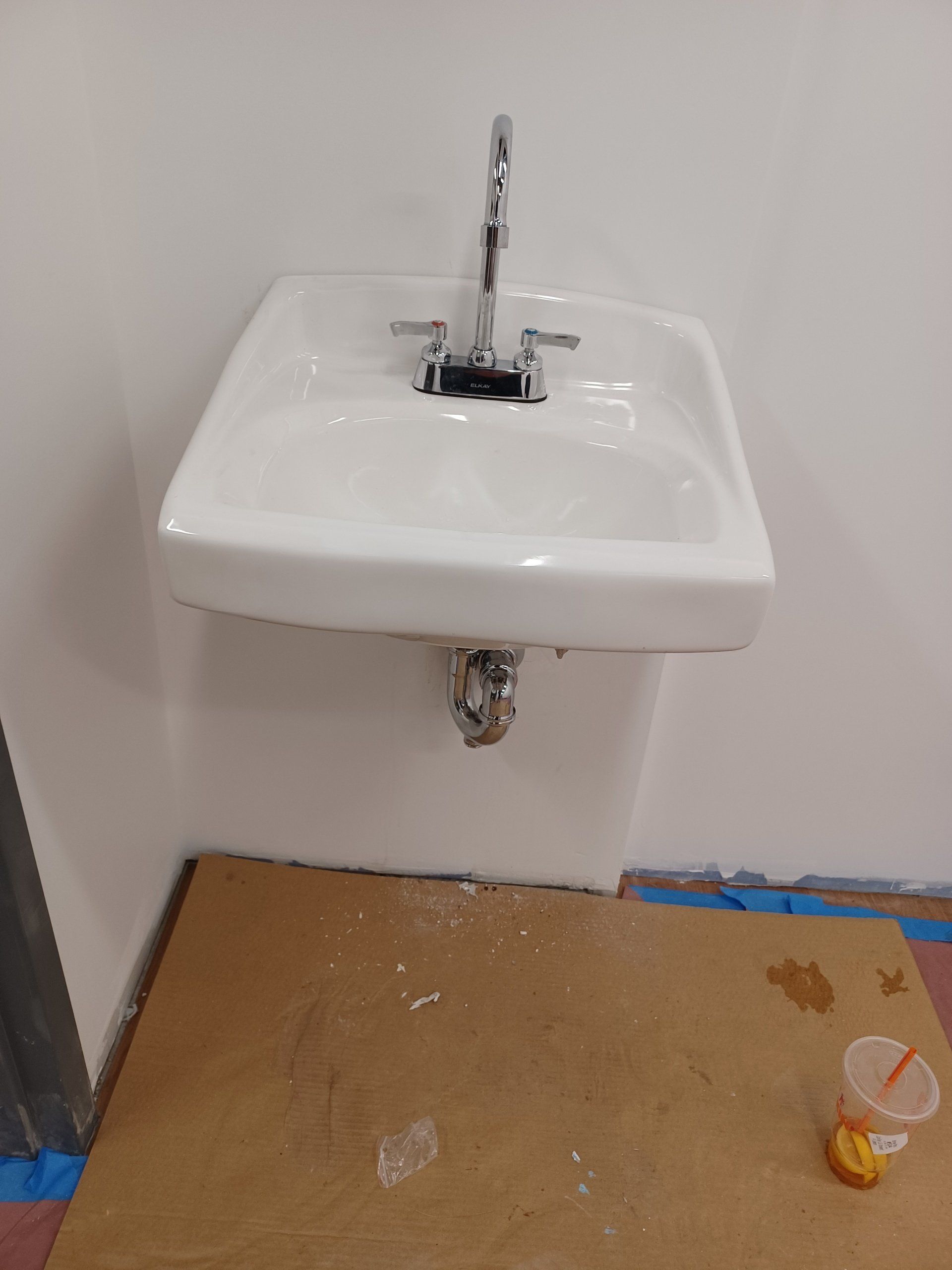 White wall-mounted sink with chrome faucet, set in a corner with cardboard on the floor.