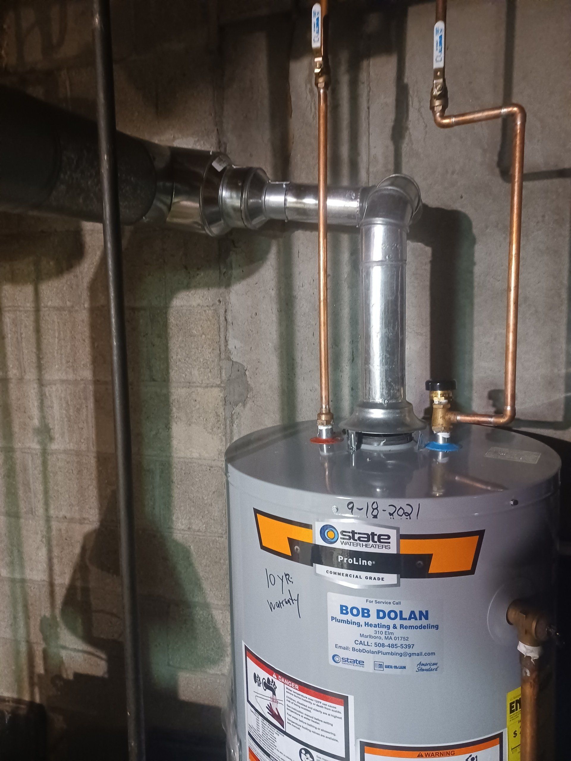 Water heater with copper pipes and vent in a concrete-walled basement.