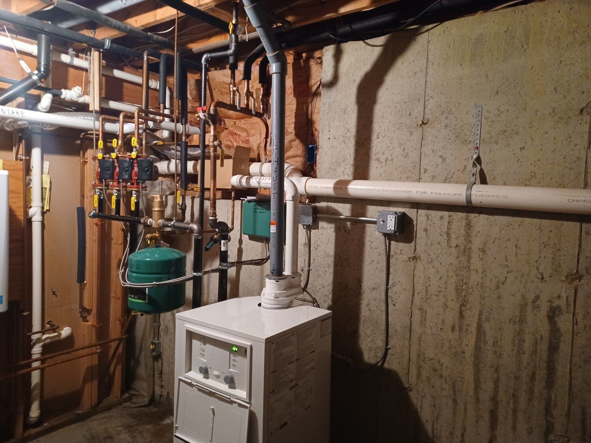 Basement with furnace, pipes, and electrical box on a concrete wall.