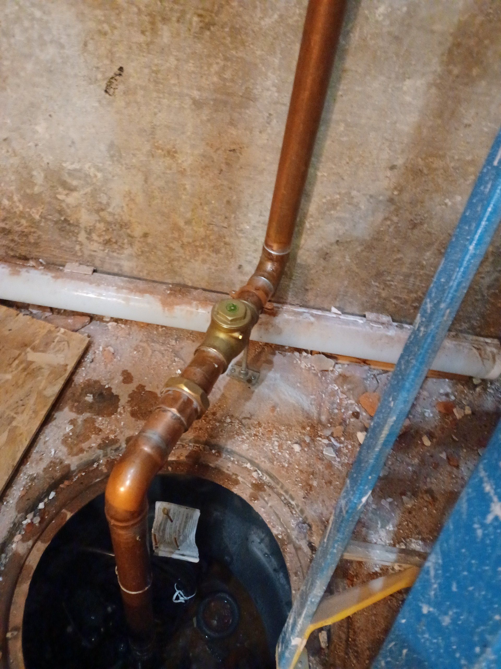 Copper pipes with a brass valve over a dark circular opening.
