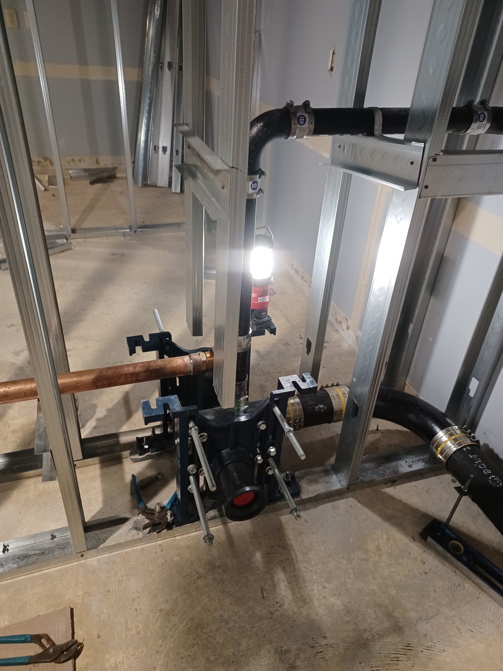 Plumbing rough-in within a metal stud wall. Black drain pipes, copper water pipes, and a flush valve are visible.