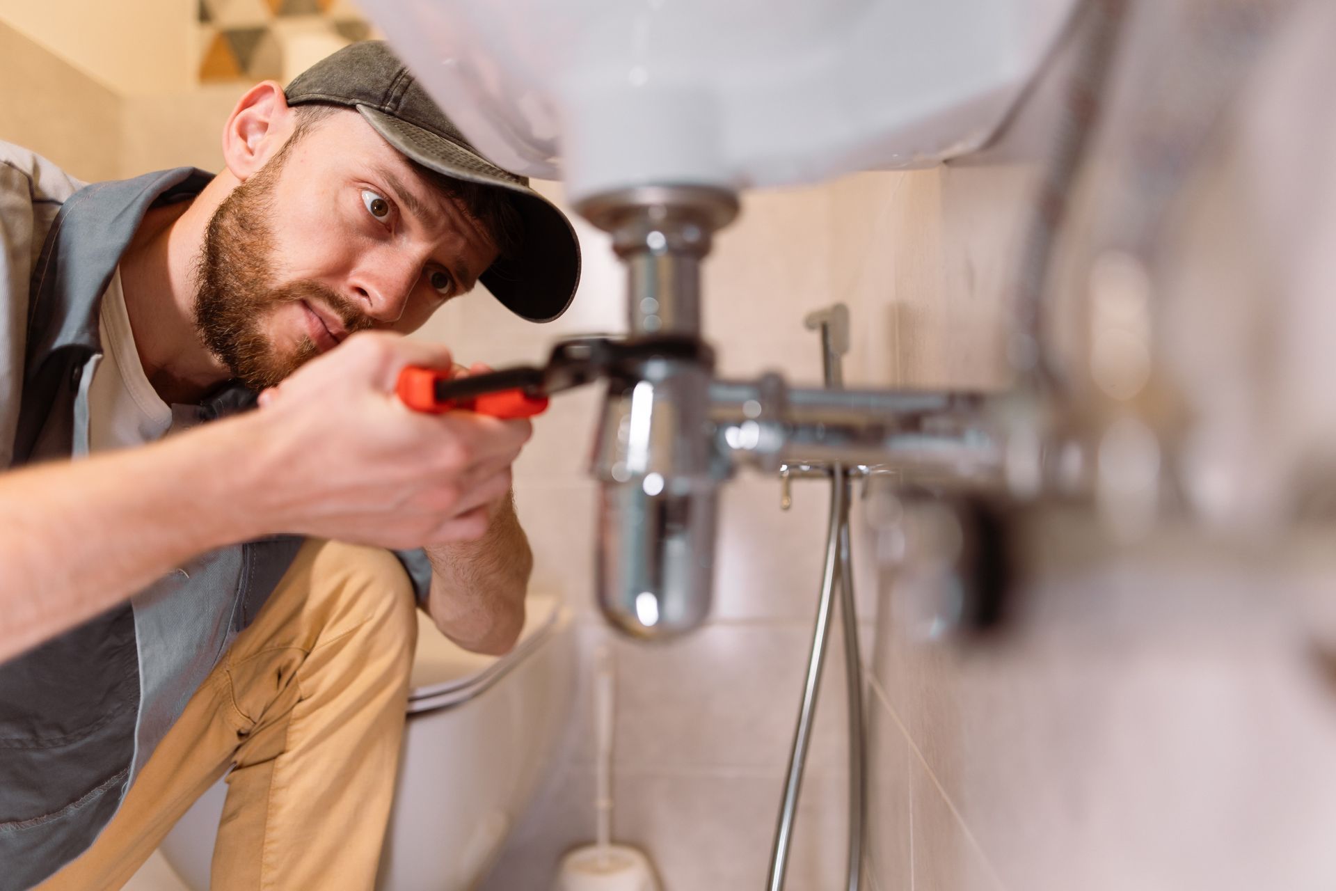 A man in a bathroom repairing a sink with a special wrench, showcasing a plumber's work.