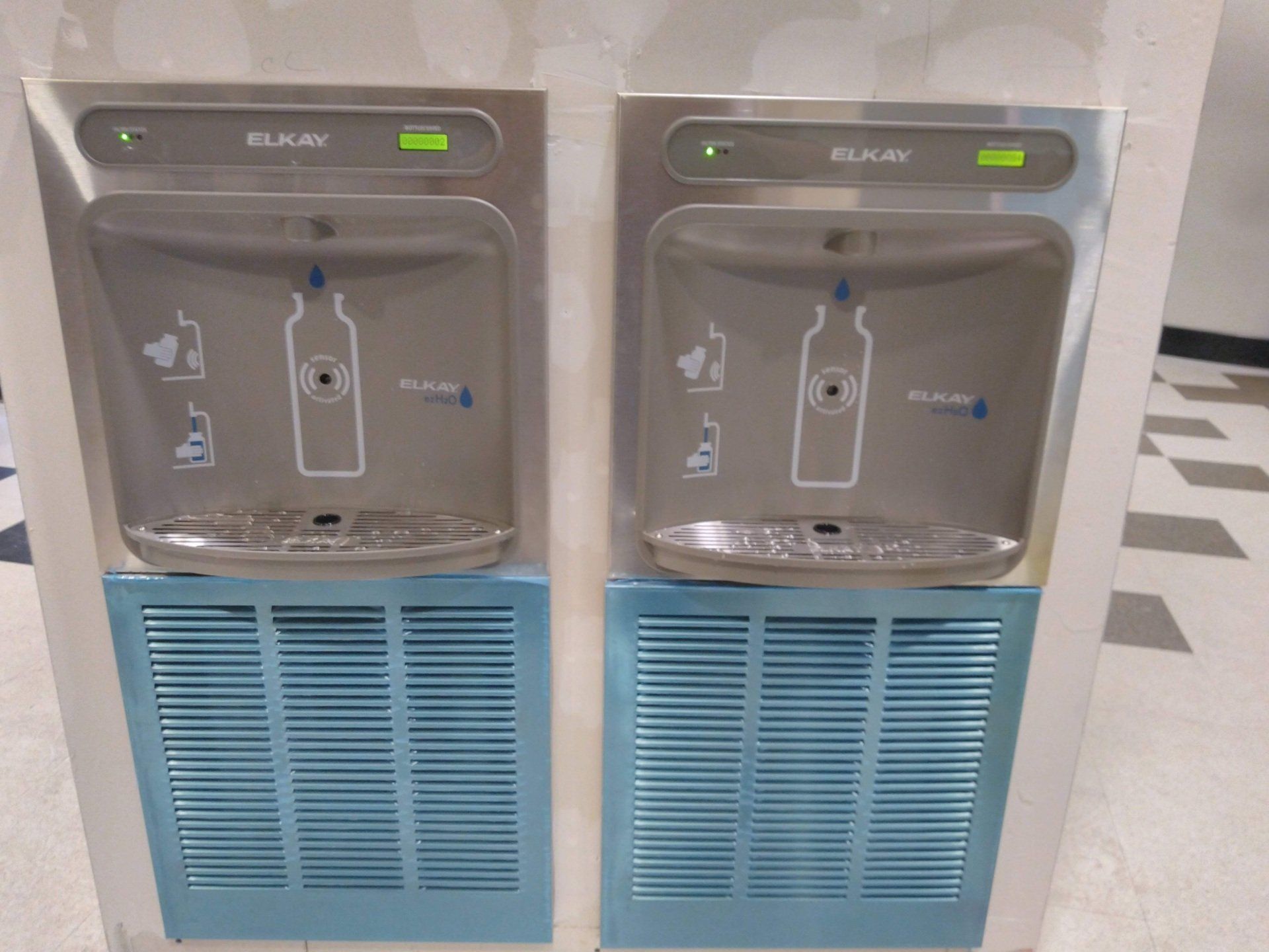 Two Elkay water bottle filling stations. Stainless steel, blue vents, green lights.