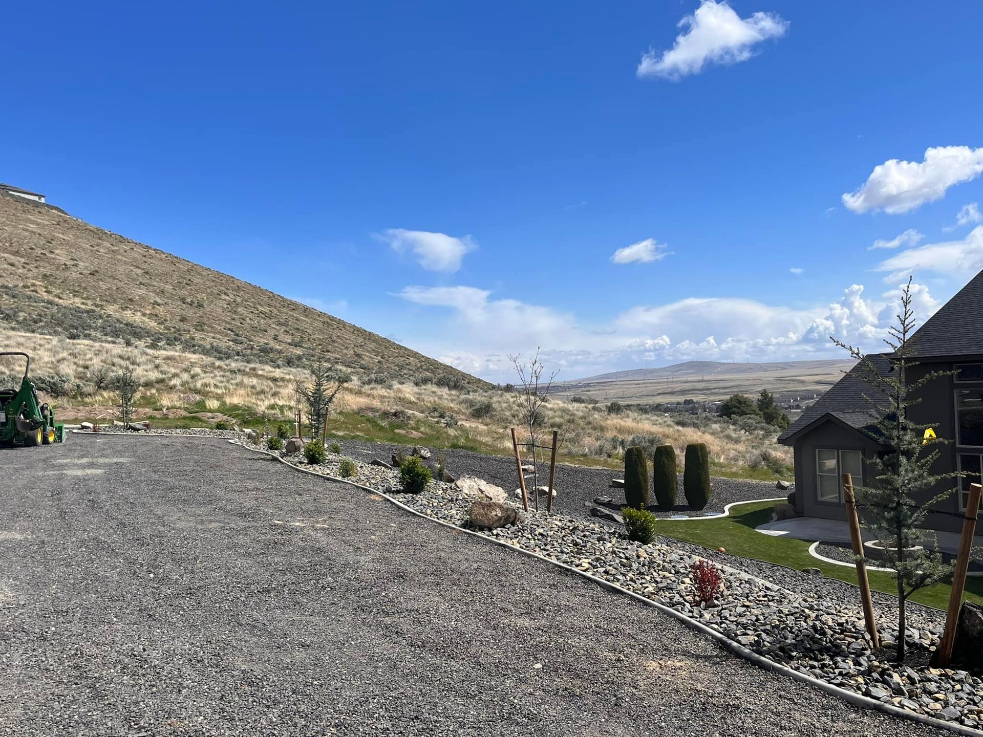 A gravel driveway leading to a house on top of a hill.
