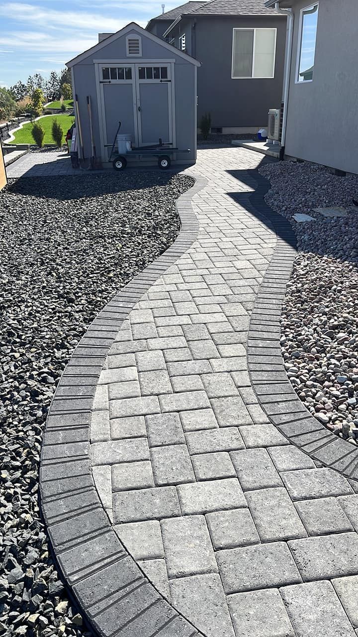 A brick walkway leading to a house with a shed in the background.
