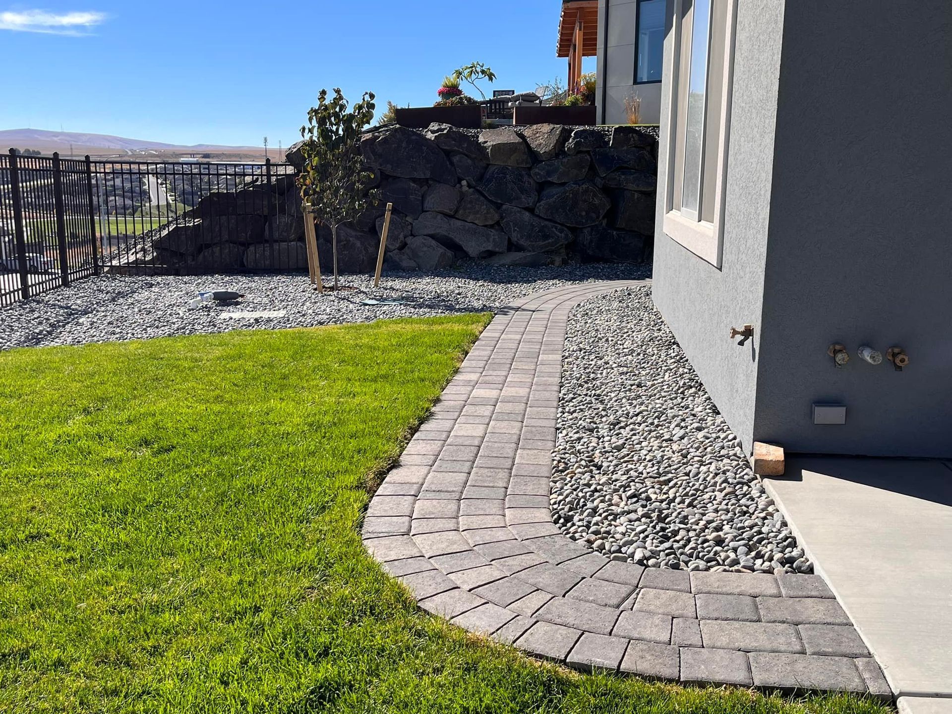 A brick walkway leading to a house next to a lush green lawn.